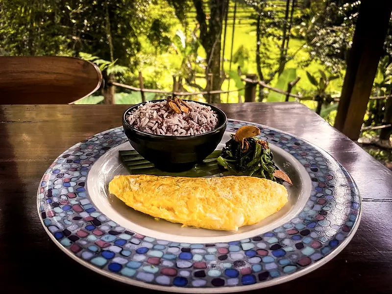 Breakfast of eggs, red rice and greens on a patterned plate
